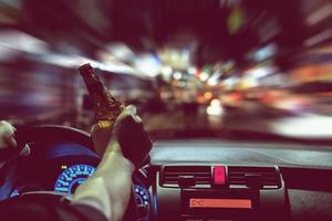 homem bebe cerveja enquanto dirige à noite na cidade perigosamente, sistema de volante à esquerda foto
