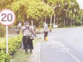 homem de trabalho usando máquina de corte de grama perto da estrada foto