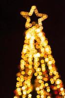 borrão suave de luz bokeh, árvore de natal e estrela no topo, sobre fundo preto foto