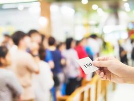 mão masculina segurando o cartão de fila sobre longas filas esperando pessoas foto