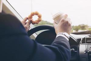 homem comendo rosquinhas com café enquanto dirige o carro - conceito de condução insegura multitarefa foto