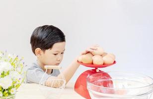 um menino está pesando ovos crus, preparando-se para fazer um bolo. foto