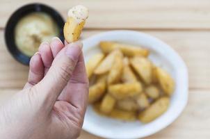 mão segurando batata frita com molho sobre fundo desfocado. foto