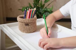 mãos de criança desenhando com lápis de cor e cesta de vime tecida para armazenamento de artigos de papelaria. cesta feita à mão para pedido de mesa. vista de corte. foto