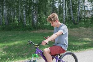 menino adolescente encaracolado andando de bicicleta e mensagens de texto. foto