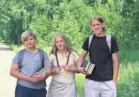 retrato de um grupo de adolescentes de várias alturas com mochilas e livros sorrindo e olhando para a câmera, adolescentes em um parque com árvores verdes de verão em um fundo foto