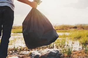 mão segurando o saco preto de lixo no rio para limpeza com pôr do sol foto