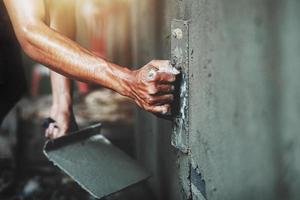 mão fechada do trabalhador rebocando cimento na parede para construir casa foto