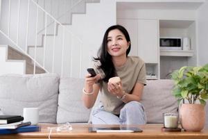 bela jovem asiática assistindo filme divertido na televisão em casa. garota casual atraente sinta-se feliz e relaxe, sente-se no sofá se divertindo assistindo vídeo de comédia na tv em casa. conceito de estilos de vida de atividade foto