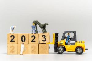 equipe de trabalhadores em miniatura cria o número 2023 no bloco de madeira foto