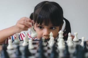 menina asiática jogando xadrez em casa. um jogo de xadrez foto