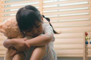 close-up menina solitária abraçando o brinquedo, sentado em casa sozinho, chateado criança infeliz esperando pelos pais, pensando em problemas, mau relacionamento na família, trauma psicológico foto