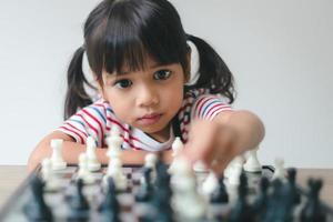 menina asiática jogando xadrez em casa. um jogo de xadrez foto