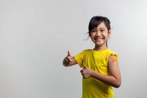 covid 19 vacinas para o conceito de crianças. estúdio um retrato de uma adorável garota asiática depois de receber sua primeira dose de vacina. imune, seguro, disponível, de volta às aulas. foto