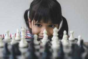 menina asiática jogando xadrez em casa. um jogo de xadrez foto