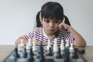 menina asiática jogando xadrez em casa. um jogo de xadrez foto