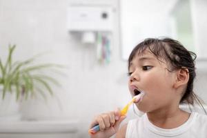 menina bonitinha limpando os dentes com uma escova de dentes no banheiro foto