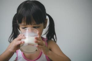 menina asiática está bebendo leite de um copo ela estava muito feliz. foto