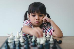 menina asiática jogando xadrez em casa. um jogo de xadrez foto