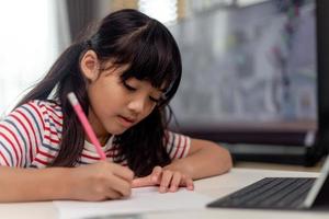 linda criança asiática aprendendo aula de estudo on-line com videochamada do tablet em casa conceito de distanciamento social foto