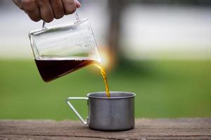 jovem derramando café na xícara, café da manhã ao ar livre. viajante acampando pela primeira vez, nova experiência para descansar com barraca. natureza, lazer, sem pressa, conceito de paz e tranquilidade foto