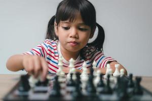 menina asiática jogando xadrez em casa. um jogo de xadrez foto