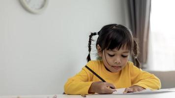 estudante de criança asiática de volta à escola ou sorriso de menina criança escreva uma nota ou desenhe a lápis e leia em um tablet de computador fazendo lição de casa para uma nova ideia pensar ou as pessoas aprendem em casa