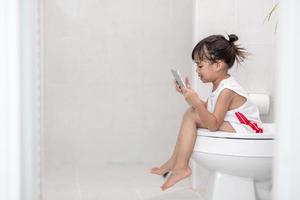 criança sentada no vaso sanitário segurando o tablet. conceito de smartphone viciado em criança foto