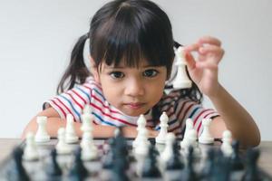 menina asiática jogando xadrez em casa. um jogo de xadrez foto