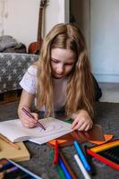 a garota depois da escola brinca em casa, desenha com lápis e canetas hidrográficas foto