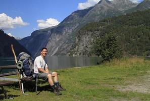 alpinista com mochila fazendo uma pausa ao lado de um fiorde na noruega foto