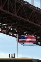 bandeira americana balançando ao vento ao lado da ponte golden gate em san francisco, califórnia foto