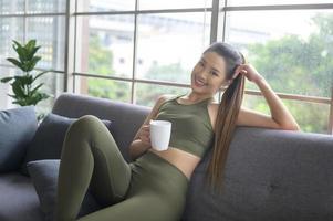 mulher jovem fitness em roupas esportivas tomando uma xícara de café depois de se exercitar em casa, saudável e estilos de vida. foto