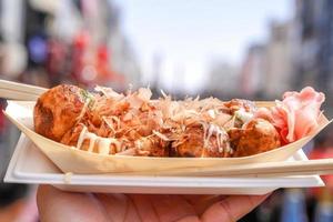 takoyaki, bola de carne de polvo japonês local na mão com paisagem urbana desfocada, pronta para comer. foto