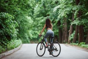 bicicleta novinha. ciclista feminina na estrada de asfalto na floresta durante o dia foto