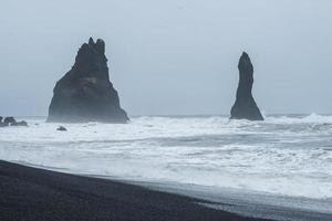 reynisfjara ou a praia de areia preta do sul da Islândia com a icônica formação rochosa reynisdrangar em clima dramático e céu. foto