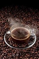 copo de café preto quente com pires de vidro coloque na pilha de sementes de café. café escuro quente e vapor. fechar-se. vista do topo. foto
