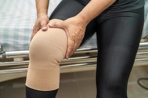 paciente mulher asiática toca e sente dor no joelho, conceito médico saudável. foto