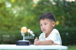 menino asiático joga equipamentos de aprendizagem de brinquedos do sistema solar durante nova mudança normal após coronavírus ou situação de pandemia de surto pós covid-19 foto