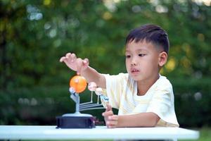 menino asiático vivendo brinquedos do sistema solar, equipamento de aprendizagem em casa, durante nova mudança normal após coronavírus ou situação de pandemia de surto pós covid-19 foto