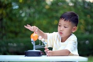 menino asiático vivendo brinquedos do sistema solar, equipamento de aprendizagem em casa, durante nova mudança normal após coronavírus ou situação de pandemia de surto pós covid-19