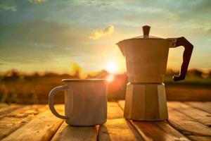 xícara de café quente e pote de moka com fundo do nascer do sol. foto