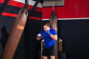 boxer homem exercitando socos com saco de boxe no ginásio, boxer batendo um enorme saco de pancadas em um estúdio de boxe foto