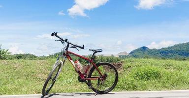 bicicleta de montanha vermelha na estrada rural e as nuvens no céu azul foto