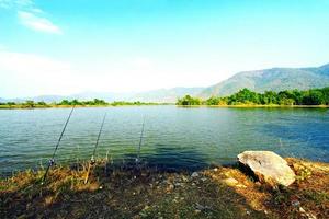 três varas de pesca com belo lago, montanhas e fundo de céu azul. ferramenta para pegar peixes e conceito de esporte foto