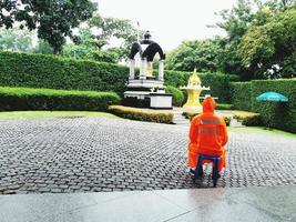 bangkok, tailândia - 11 de setembro de 2017 guarda de segurança sentado e vestindo capa de chuva laranja para ficar alerta e controlar a entrada ou saída de pessoas para a área no dia chuvoso foto