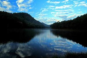 céu azul e nuvens reflexão no lago com montanha e floresta em pangoung, tham pla. parque nacional pha suea, mae hong son, tailândia foto