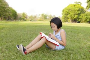 menina asiática lendo livro no parque foto