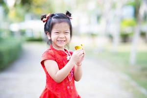 retrato linda garota asiática segurando chinês dourado. doces crianças sorridentes estão felizes. criança comemora o ano novo chinês. garoto estava vestindo um lindo qipao cheongsam vermelho. fêmea de 5 anos. foto