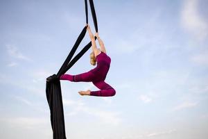 exercícios com seda aérea ao ar livre, fundo do céu. bela mulher em forma de treinamento acrobático no ar. foto